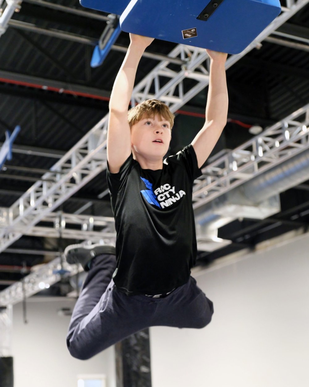 Young ROC City Ninja athlete hanging from a grip on the ninja rig