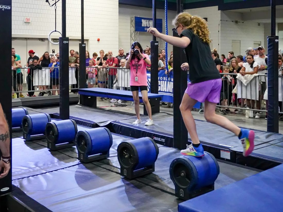 Girl crossing the rolling logs on the ninja course